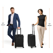 A 60 man in a blue suit and a 58 woman in a black sleeveless top and beige pants stand confidently with their Briggs & Riley Baseline Essential 22 Carry-On Expandable Spinners, ready for CX expansion.