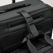 Close-up of the black Briggs & Riley Baseline Essential 22 Carry-On Expandable Spinner with a sturdy handle, buckle strap, and visible logo tag. It features CX expansion, multiple compartments, and zippers for functionality and durability.