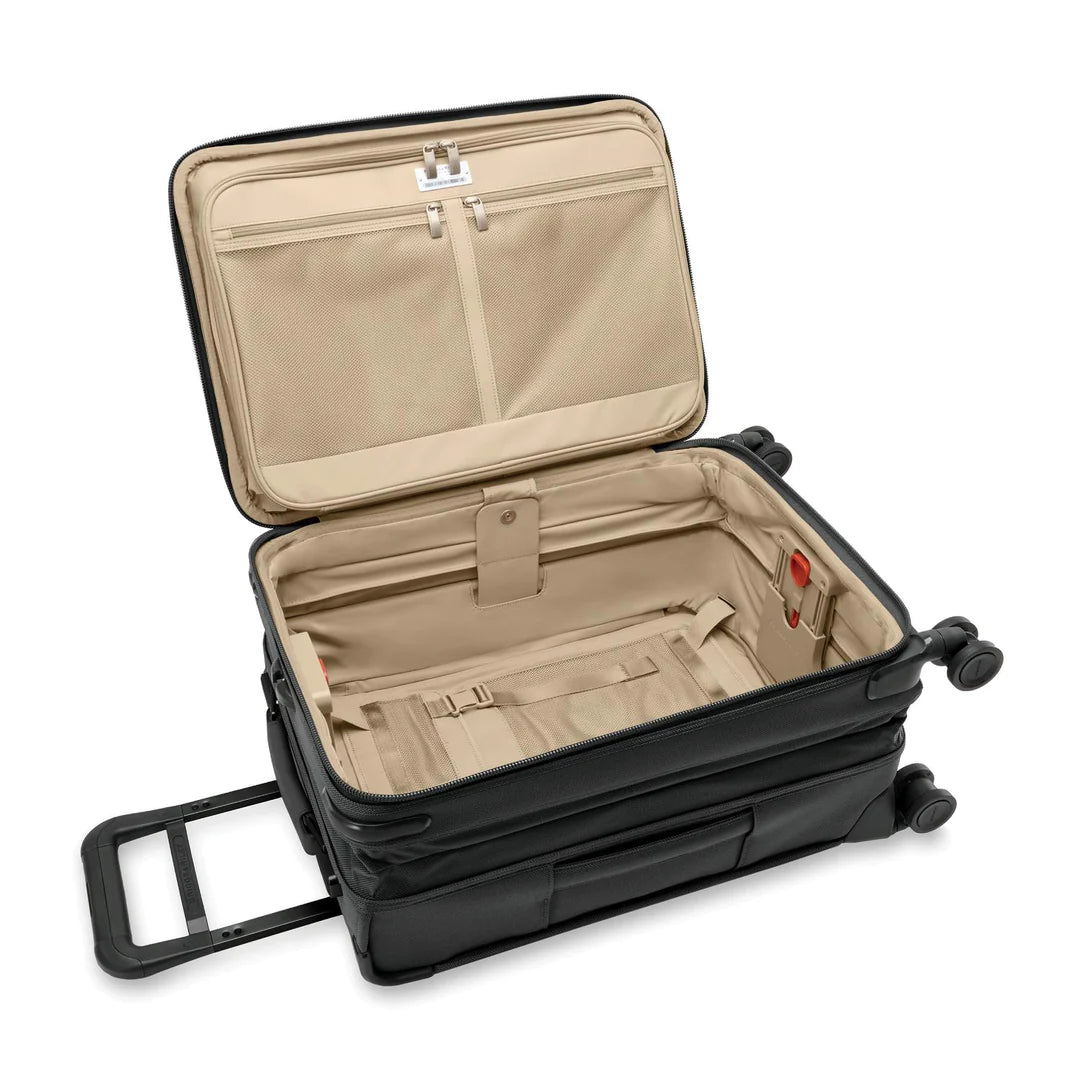 Open the Briggs & Riley Baseline Essential 22 Black Carry-On Spinner to reveal a beige interior with two mesh lid pockets, adjustable main compartment straps, and a garment folder for wrinkle-free travel. It features four wheels and a retractable handle for smooth movement.