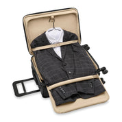 The Briggs & Riley Baseline Essential 22 Carry-On Expandable Spinner in black reveals a neatly packed grey checked suit and white dress shirt, secured with beige straps. It features a garment folder design, retractable handle, and four smooth-rolling wheels for easy travel.