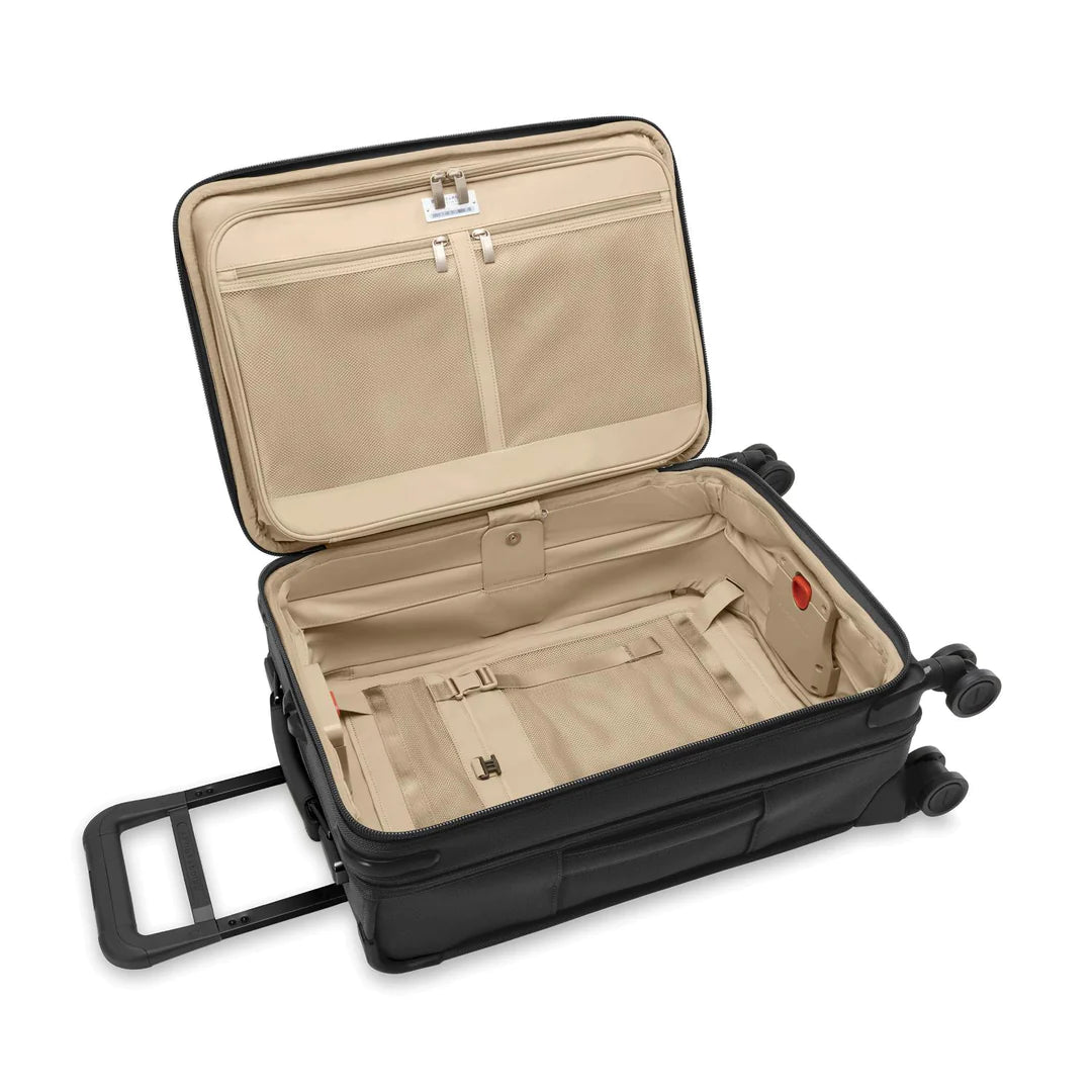 The Briggs & Riley Baseline Essential 22 Carry-On Expandable Spinner features a black design with a beige interior, multiple pockets, a garment folder, and straps for organization. It has four wheels and an adjustable pull handle for effortless travel.